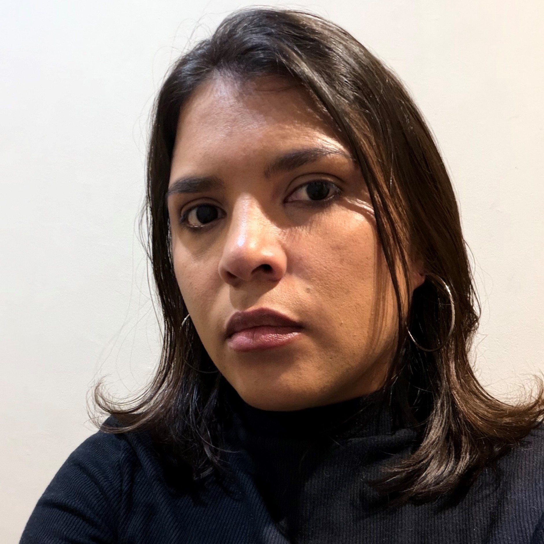 Close-up of a young woman's face cropped at the nose and hair, wearing a dark turtleneck against a light background, looking slightly to the left.