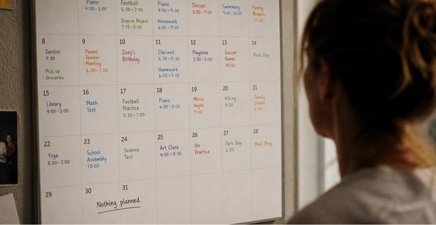 Person standing in front of a large wall calendar filled with daily notes and events for the month, including school activities and appointments.